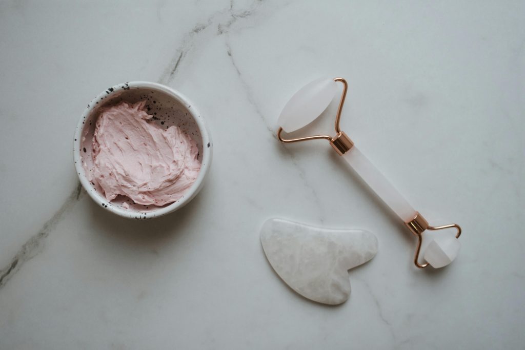 Top view of gua sha tools and pink facial cream on a marble countertop.